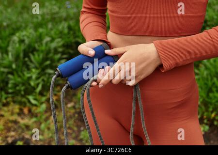 Eine junge Frau in sportlicher Kleidung bereitet sich darauf vor, in üppigem Grün mit Seilen zu springen und sich fit zu machen. Stockfoto
