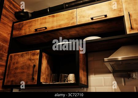 Rustikale Küchenschränke aus Holz mit schwarzem Rahmen und freiliegenden Regalen mit weißem Geschirr und Glas. Stockfoto