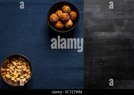 Schwarze Schüssel mit Walnüssen und blauem Tischtuch auf schwarzem Tafel Hintergrund. Flache Lagen. Draufsicht. Stockfoto