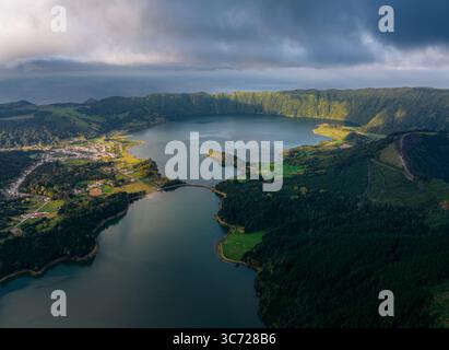 Blick aus der Vogelperspektive auf zwei Kraterseen, die die Stimmung des Himmels widerspiegeln, eingebettet in grüne Hügel und schattige Wälder, Miradouro da Vista do Rei, Ponta Delgada, Portugal. Stockfoto