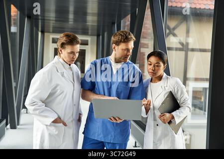 Drei medizinische Fachkräfte führen eine Diskussion, während sie einen digitalen Bericht prüfen. Stockfoto