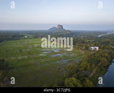 Aus der Vogelperspektive auf die majestätische Felsenfestung Sigiriya, die sich über einer grünen Landschaft aus Reisfeldern und dichten Wäldern erhebt, Sigiriya, Sri Lanka. Stockfoto
