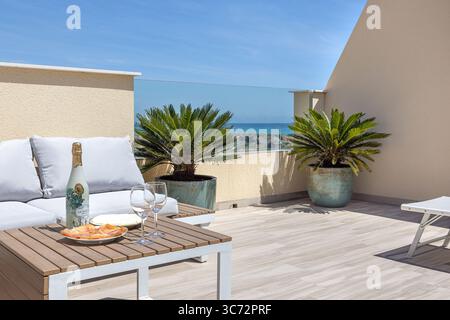 Geräumige Dachterrasse mit Meerblick, bequemen Sitzgelegenheiten und tropischen Pflanzen - der perfekte Ort zum Sonnenbaden und Weintrinken. Stockfoto