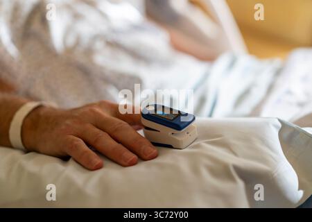 Nahaufnahme der Hand des Patienten mit Pulsoxymeter zur Überwachung der Sauerstoffsättigung im Krankenhaus. Stockfoto