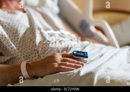 Patient im Krankenhausbett mit Pulsoxymeter zur Überwachung der Vitalparameter. Stockfoto