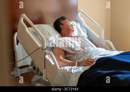 Mann, der in einem Krankenhausbett liegt und aus dem Fenster blickt. Stockfoto