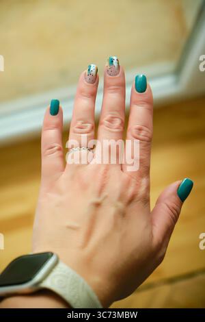 Eine Nahaufnahme einer trendigen weiblichen Maniküre mit blaublauem und abstraktem Nailart mit schwarzen Punkten und Goldfolie Stockfoto