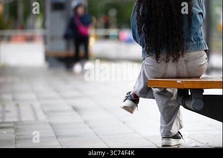Stuttgart, Deutschland. August 2025. Eine junge Frau sitzt auf einer Bank an einer Bushaltestelle. Im Hintergrund steht eine andere Person auf. Quelle: Markus Lenhardt/dpa/Alamy Live News Stockfoto