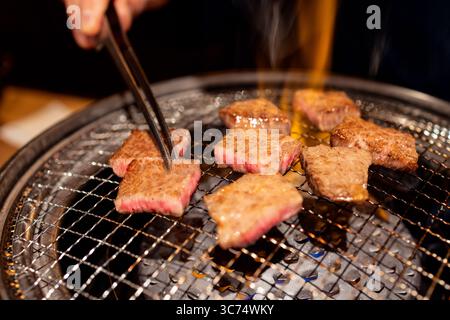 Grillen von A5-Wagyu-Rindfleischschnitten auf einem Metallrost über offener Flamme mit saftiger Marmorierung und appetitlicher Oberfläche im japanischen Yakiniku-Stil Stockfoto