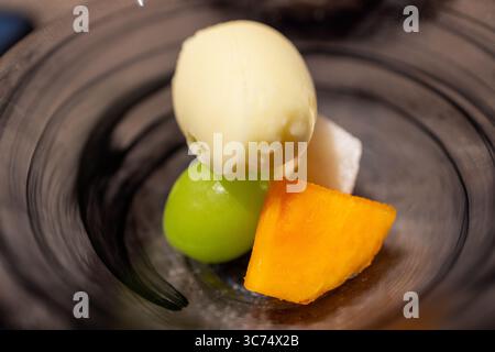 Dessertschüssel mit cremigem Eis, frischer Mangoblättung und Traube in einer minimalistischen süßen Präsentation Stockfoto