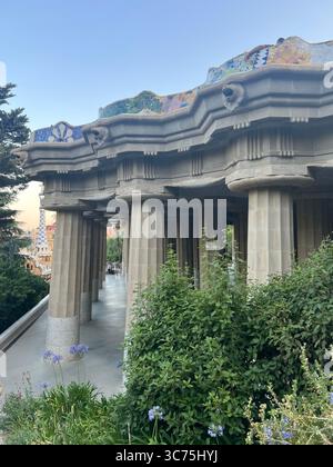 Blick auf die Hypostyle Halle vom hinteren Eingang des Park Güell, mit den dorischen Säulen von Gaudí und dem ikonischen Mosaikbalkon darüber, Barcelona, Katalonien Stockfoto