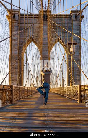 Bridge Yoga Sunrise Serenity: Eine Person findet ihr Zentrum mit einer Yoga-Pose auf der Brooklyn Bridge, die 1883 fertiggestellt wurde. Das Licht am frühen Morgen Stockfoto