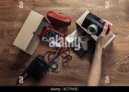 Weibliche Hände stapeln Retro-Objekte in einem Karton auf einem Holzboden. Antiquitäten, Vintage. Draufsicht Stockfoto
