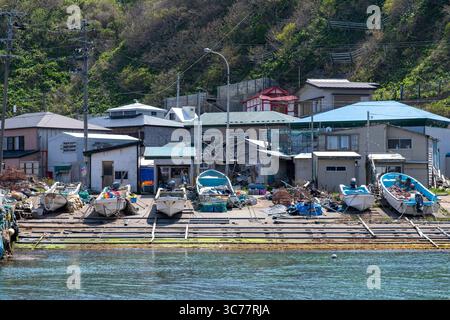 Kap TAPPI, Japan-1. Mai 2025; Fischerboote, die auf dem abschüssigen Pier des TAPPI-Fischeranlegens mit Häusern eines kleinen Fischerdorfes im Nordwesten verankert sind Stockfoto