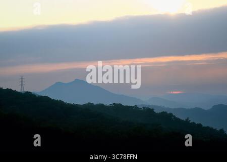 Atemberaubender Sonnenaufgang über dem Wuzhishan Berg in Xizhi, New Taipei City, mit sanften Orange- und Rosa-Tönen, die die nebeligen Hügel und die Silhouette der Stromleitung beleuchten Stockfoto