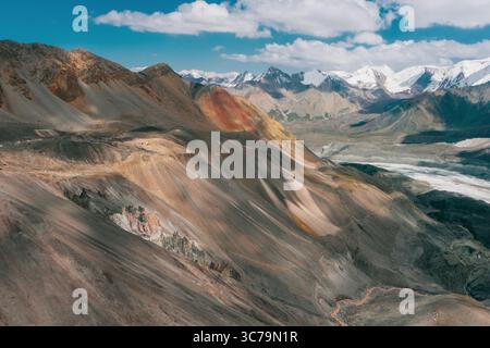 Luftaufnahme des malerischen, mehrfarbigen Weitwinkels Pamir und des sanften Lichts- und Schattengebirges Tals mit schneebedeckten Gipfeln im Hintergrund. Kirgisistan Stockfoto