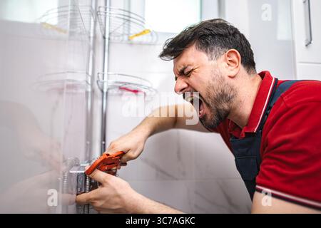 Frustriertes Schreien des Klempners beim Festziehen des Rohrs im Badezimmer Stockfoto