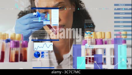 Afroamerikanischer Wissenschaftler im Laborkittel, der Blut im Reagenzglas auf dem Labortisch untersucht, Datenüberlagerungen Stockfoto