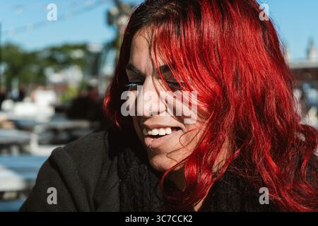 Porträt einer fröhlichen Frau mit leuchtend roten Haaren, die einen sonnigen Tag in einer ungezwungenen urbanen Umgebung genießt Stockfoto