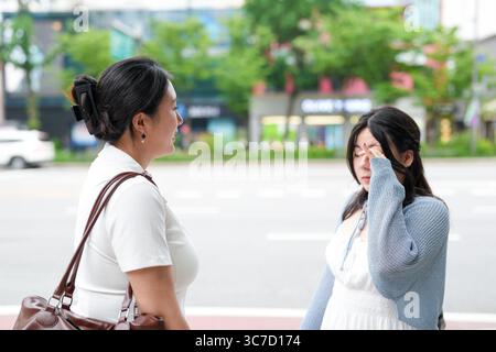 Zwei koreanische Frauen im Alter von 20 Jahren in lässiger Kleidung geben vor, auf einem Boulevard zu streiten und sehen sich mit Lächeln und kleinen Gesten an Stockfoto