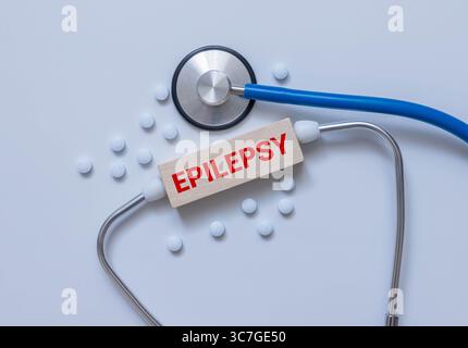 Das Wort EPILEPSIE steht auf Holzblöcken auf blauem Hintergrund in der Nähe der Pillen. Medizinisches Konzept Stockfoto