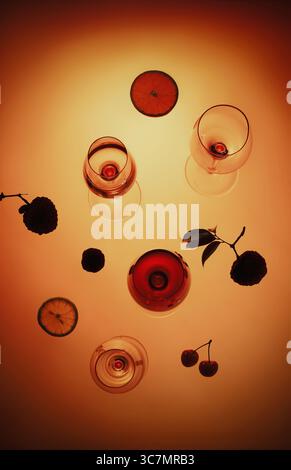 Stillleben mit Weingläsern, Früchten und Schatten in warmer Beleuchtung, Rotwein im Glas auf orangem Hintergrund. Farbton im Vintage-Stil Stockfoto
