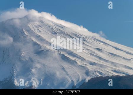Nahaufnahme des schneebedeckten symmetrischen Kegels des aktiven Stratovulkans Mt. Fuji mit ein paar Wolken weht über den Gipfel des Vulkans Stockfoto