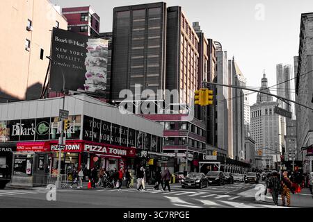 Fußgänger, Taxis und eine Pizzastadt beleben eine Kreuzung von Midtown Manhattan, die von Ziegelfassaden und Glasfassaden vor einem klaren blauen Himmel eingerahmt wird. Stockfoto