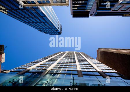 Von einer Straße in Manhattan aus blicken Glas- und Backsteintürme in den Himmel und bilden einen klaren blauen Himmel, der die legendäre Skyline umrahmt und den Puls der Stadt fängt Stockfoto