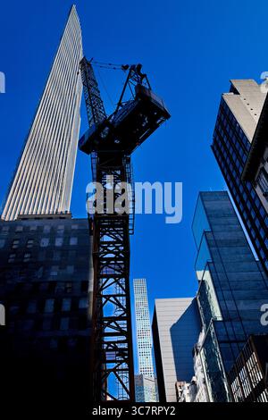 Ein Baukran steht im Schatten eines Vanderbilt Glasturms auf einer Midtown Manhattan Street und unterstreicht die vertikale Energie der Stadt. Stockfoto