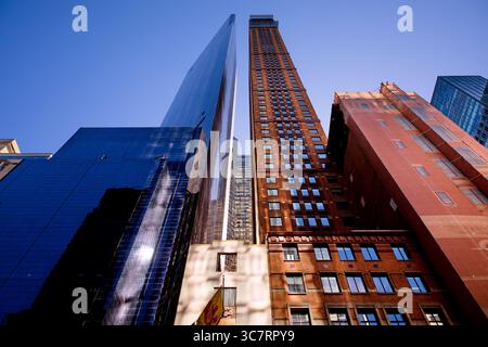 Ein Vanderbilt-Glasturm und ein Backsteinhochhaus ragen über Midtown Manhattan in einer Niedrigwinkelaufnahme auf, die Alt und Neu im Kontrast zu einem klaren Himmel stellt. Stockfoto