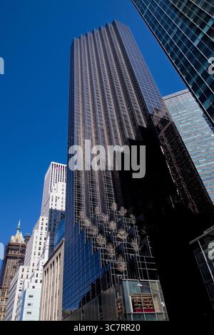 Das elegante schwarze Glas eines Hochhauses in Midtown Manhattan reflektiert die benachbarten Türme unter einem klaren blauen Himmel und fängt die gespiegelte urbane Geometrie der Stadt ein. Stockfoto