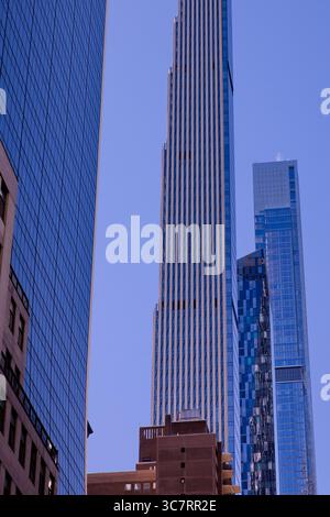 Die schlanke Silhouette des Steinway Tower erhebt sich über dem Straßenschlucht von Midtown Manhattan, dessen gewellte Fassade das Licht vor dem strahlend azurblauen Himmel einfängt. Stockfoto