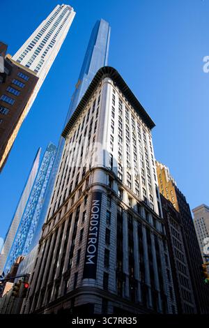 Nordstroms elegante Flaggschiff-Fassade an der 57th Street in Midtown Manhattan wird von superhohen Glastürmen flankiert, die von einem hellen azurblauen Himmel eingerahmt werden. Stockfoto
