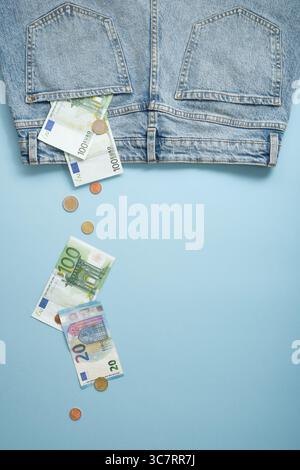 Geldscheine und Münzen fliegen aus den hinteren Taschen der blauen Jeans. Ein blauer Hintergrund, ein Ort für Ihre SMS. Stockfoto