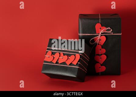 Zwei schwarze Geschenkschachteln mit roten Papierherzen auf rotem Hintergrund. Geschenke zum Valentinstag. Stockfoto
