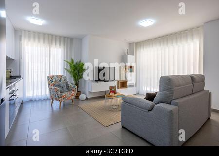 Moderner, offener Wohnbereich mit einer weichen grauen Couch, Fernseher und Essbereich im Freien durch große Schiebetüren. Stockfoto