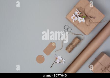 Geschenkbox in braunem handwerklichem Papier, verziert mit blühendem Apfelzweig. Umwickeln von Materialien auf hellgrauem Hintergrund. Der Frühling präsentiert die Vorbereitung. Stockfoto