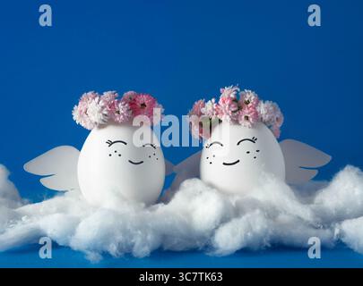 Zwei Engel in Blumenkränzen auf den Wolken. Dekorierte Ostereier. Blauer Hintergrund. Stockfoto