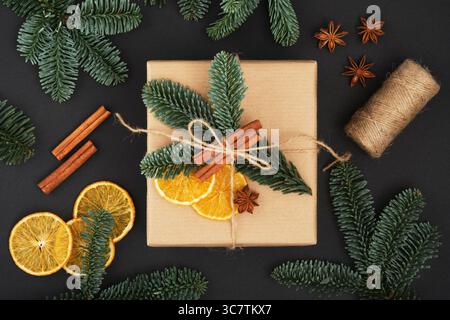 Handwerkliche Geschenkbox mit Orangen, Fichtenzweigen und Zimt auf dunklem Hintergrund. Geschenkverpackung Idee, diy. Draufsicht. Stockfoto