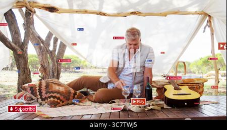 Liegender, erwachsener Mann, der drei Weingläser unter weißem Vordach auf hölzerner Plattform mit Gitarre anfasst Stockfoto