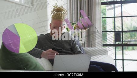 Mit Kreditkarte, Dreadlocked Mann, der auf dem Sofa im Wohnzimmer auf dem Laptop surft, mit Kartenüberlagerungen Stockfoto
