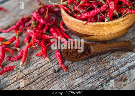 Rote Chili und Chilipulver in einer Holzschale trocknen. Roter getrockneter Pfeffer auf dunklem Holzhintergrund Stockfoto
