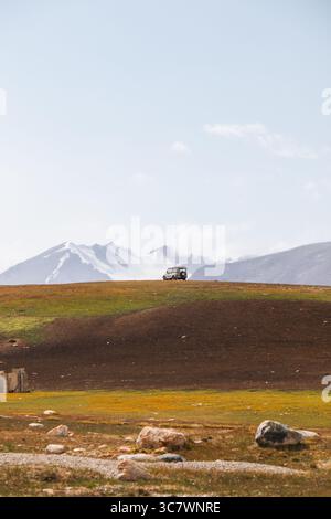 Ein weißes Geländefahrzeug sitzt auf einem abgelegenen Hügel in einer malerischen Berglandschaft mit majestätischen schneebedeckten Bergen im Hintergrund Stockfoto