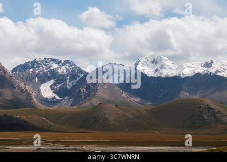 Ein Panoramablick auf ein riesiges, goldenes und grünes Tal mit majestätischen schneebedeckten Bergen im Hintergrund unter einem dramatisch bewölkten Himmel Stockfoto