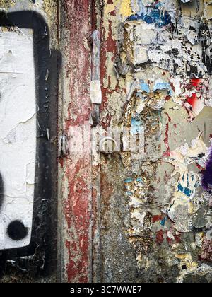 Nahaufnahme einer alten Metalltür, bedeckt mit Schichten von abblätternder Farbe, Rost und gerissenen Postern, die Texturen, Farben, und urbaner Verfall in einer Gratwanderung Stockfoto