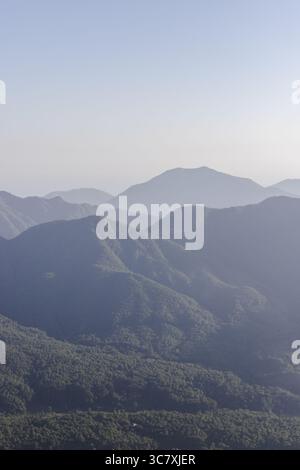 Blick auf nebelige Bergketten in Blau- und Grüntönen, die eine ruhige und ferne Landschaft unter hellem Himmel schaffen, Avellino, Kampanien, Italien. Stockfoto