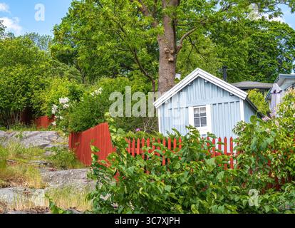 Stockholm, Schweden - 5. Juni 2025: Ein bezauberndes blaues Holzhaus, eingebettet zwischen üppigem Grün und einem roten Holzzaun. Die Szene fängt eine ruhige Natur ein Stockfoto