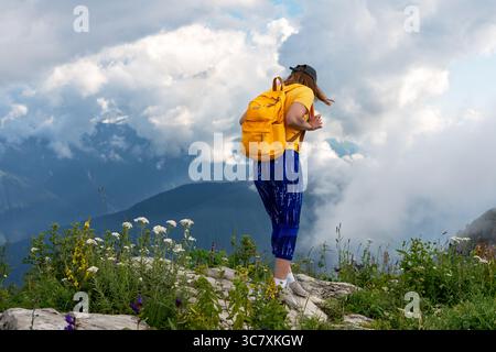 Wanderer mit gelbem Rucksack steht auf einem felsigen Gelände und blickt von einer Klippe hinunter und bewundert den atemberaubenden Blick auf die Berge, die von einem Stift umgeben sind Stockfoto