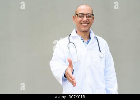 Porträt eines Reifen männlichen Glatzenarztes mit Labormantel und Brille mit Stethoskop um den Hals, posierend vor neutralem Wandhintergrund. Ideal für ihn Stockfoto